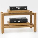 The KUNSST FURNITURE Hi Fi Audio Rack, a wooden stand with two shelves, elegantly supports a black audio amplifier on the top and a black audio component below, both equipped with buttons and dials. The rack is stylishly elevated on metal feet.