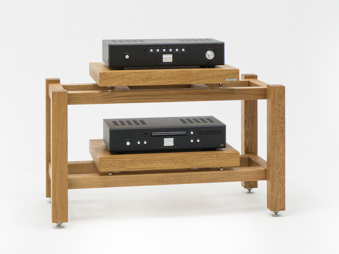 The KUNSST FURNITURE Hi Fi Audio Rack, a wooden stand with two shelves, elegantly supports a black audio amplifier on the top and a black audio component below, both equipped with buttons and dials. The rack is stylishly elevated on metal feet.