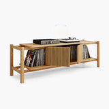 A light natural wood record player stand with open shelves, holding vinyl records and a turntable, shown on a clean white background.