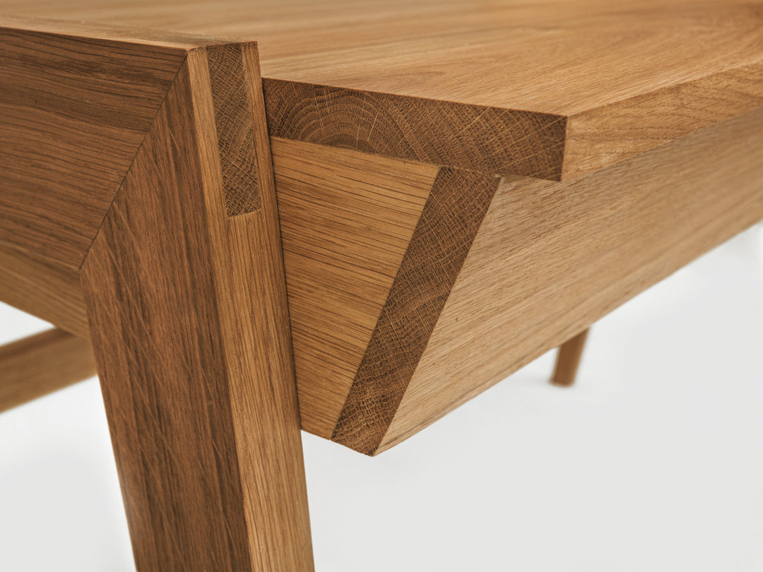 Close-up view of the Solid Oak Desk with Drawer - Model_No.01 by KUNSST FURNITURE, highlighting traditional woodworking techniques with intricate joinery and smooth, angular cuts. The natural grain emphasizes the craftsmanship and texture against a plain background.