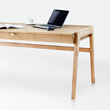 Against a white background, the Solid Oak Desk with Drawer - Model_No.01 by KUNSST FURNITURE stands prominently, highlighting traditional woodworking techniques. It features a handcrafted drawer that's slightly open, while a laptop, an open notebook with a pen, and a white coffee cup rest on top.