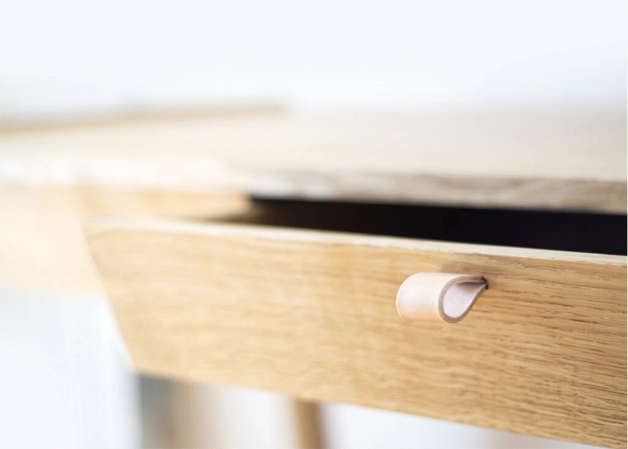 Detail of solid oak desk wooden drawer with a leather handle on a blurred white background