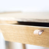 Detail of solid oak desk wooden drawer with a leather handle on a blurred white background