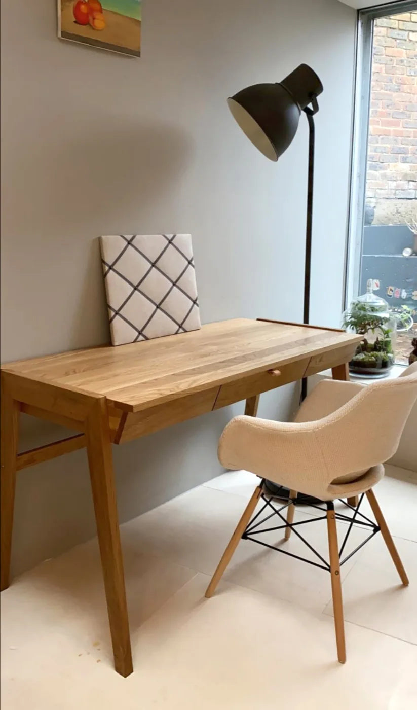 Scandinavian wooden desk with drawers standing in the corner of home office with bright armchair