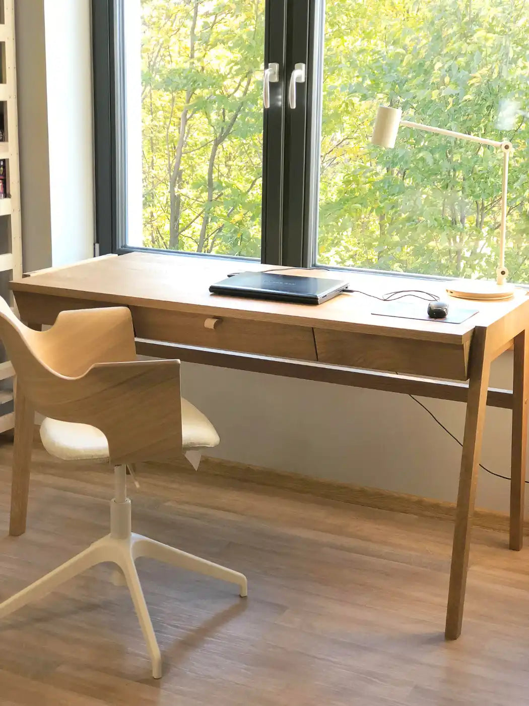 Designer writing desk with drawer standing in front of window with greener view.
